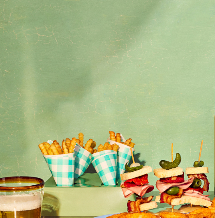 A professional happy hour scene featuring a table with beer, french fries, sandwiches, and water bottles.