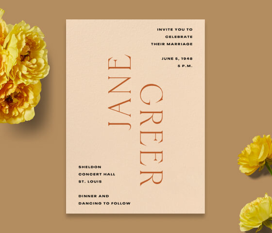 A peach typographic invitation propped with yellow ranunculus.